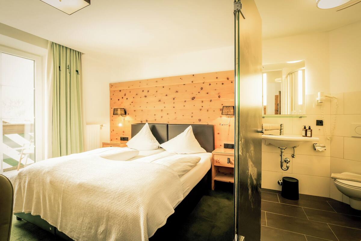 A hotel room with a bed, bedside tables, a mirror, a sink, and a toilet.