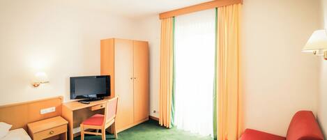 Una habitación de hotel con una cama, un escritorio con televisor, un sofá rojo y una ventana con cortinas.
