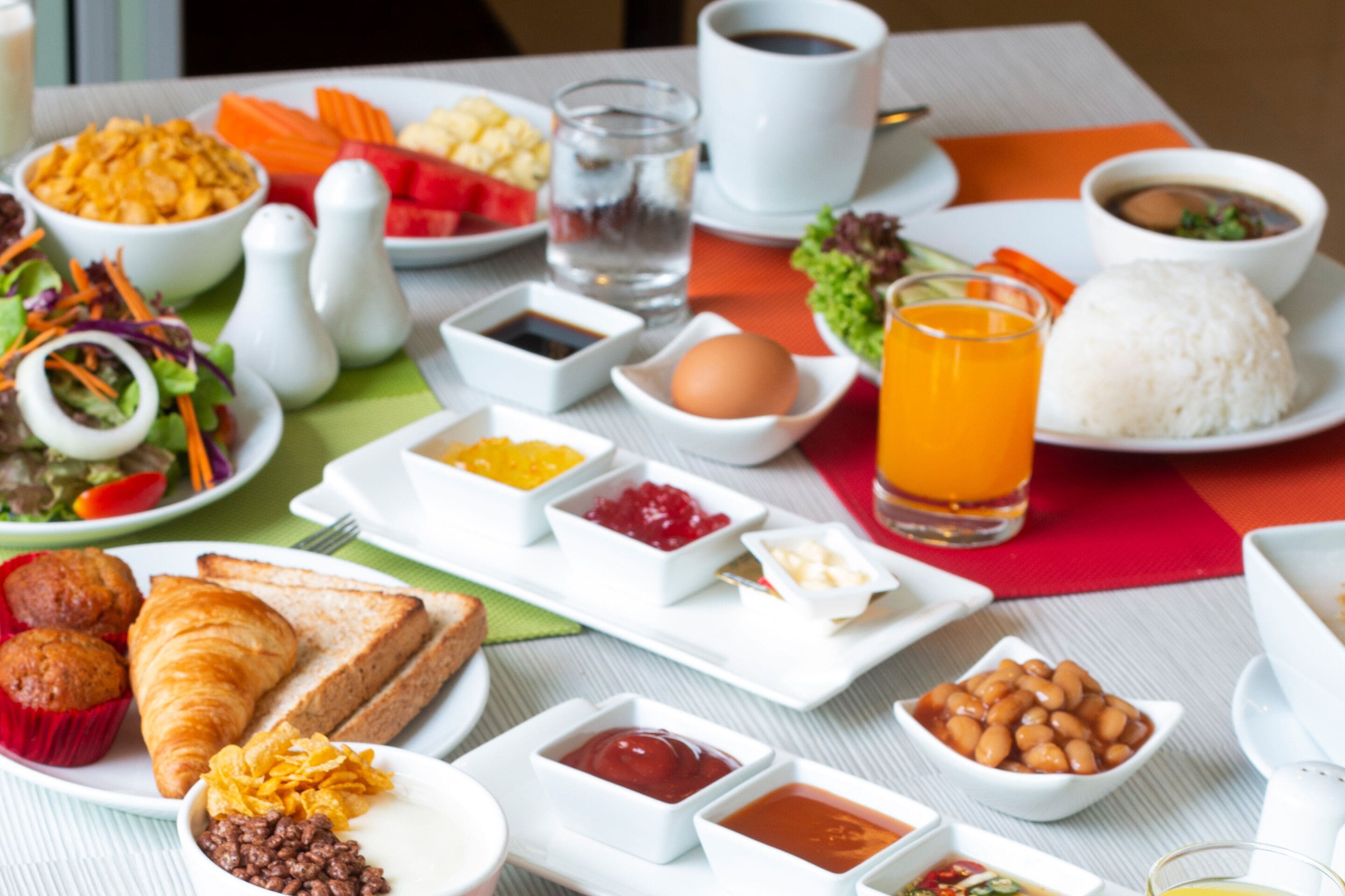 Une table dressée avec une variété d’aliments pour le petit-déjeuner, notamment des œufs, des toasts, des muffins et des boissons.