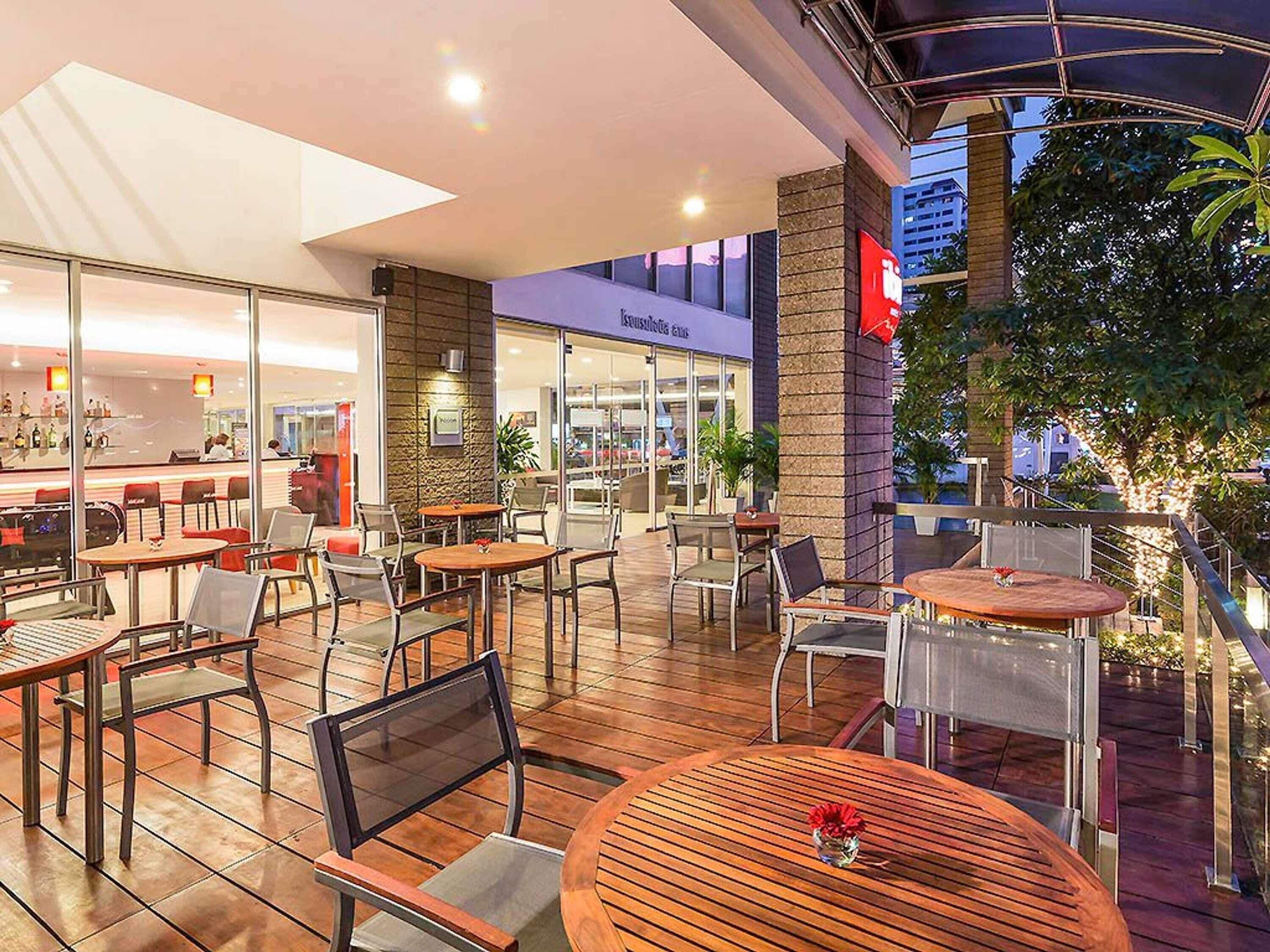 An outdoor cafe area with tables and chairs, a bar in the background, and a building with a sign.