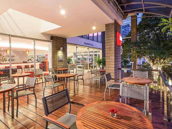 Un espace café en plein air avec des tables et des chaises, un bar en arrière-plan et un bâtiment avec une enseigne.