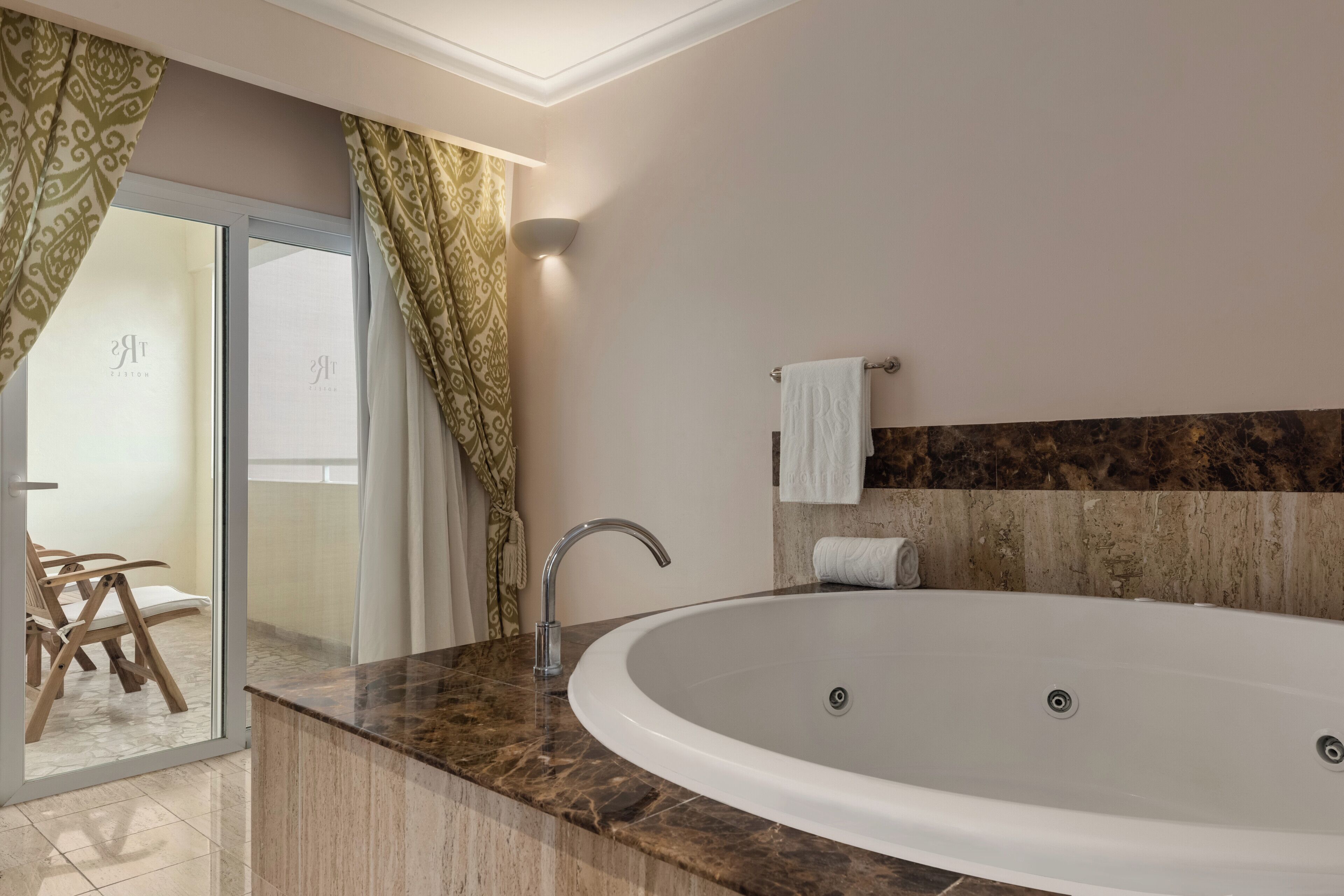 Une salle de bain moderne avec une baignoire sur pieds, une porte en verre donnant sur un balcon et un comptoir en marbre.