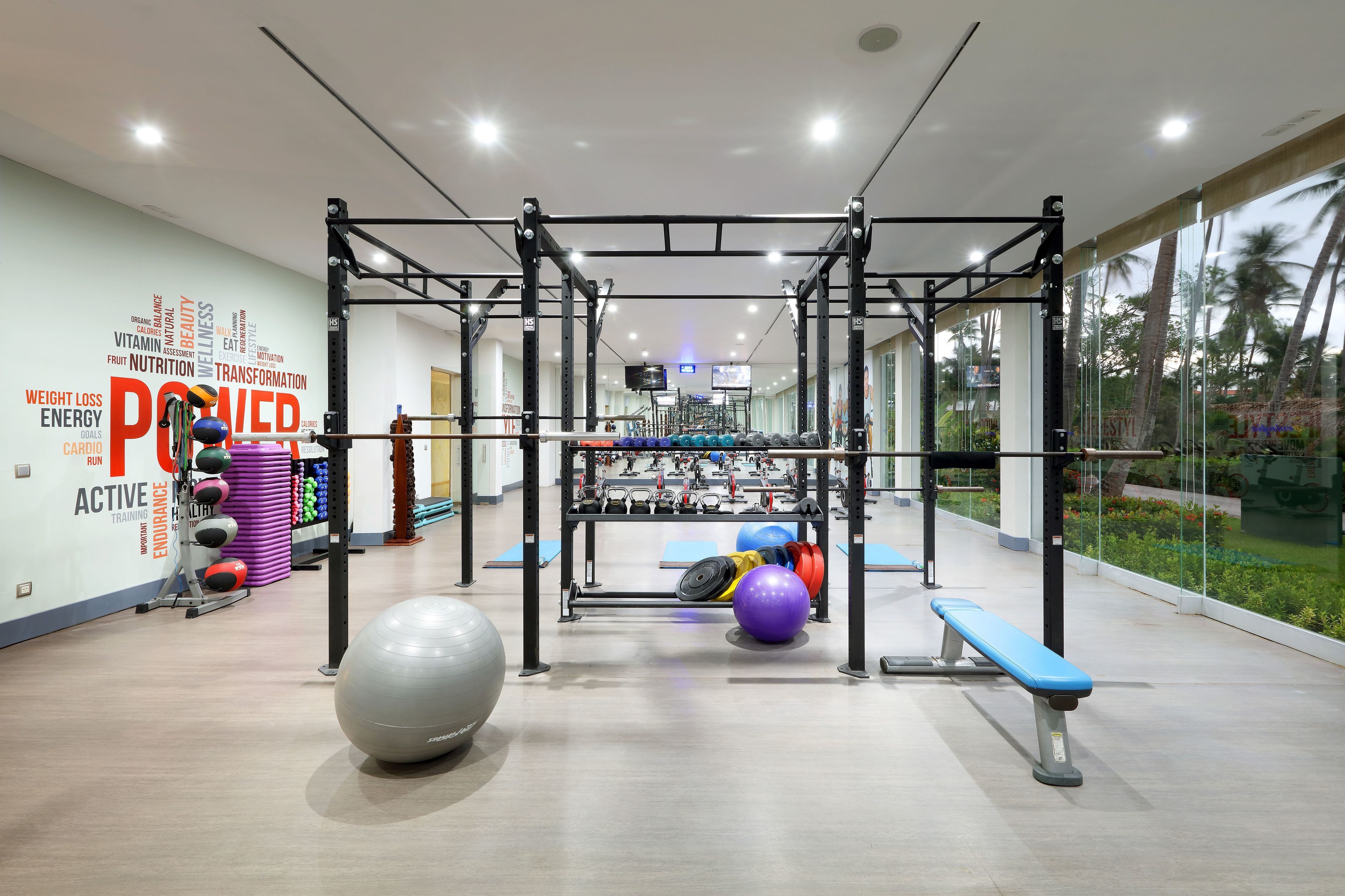 A modern gym with a pull-up bar, weight plates, and exercise balls.