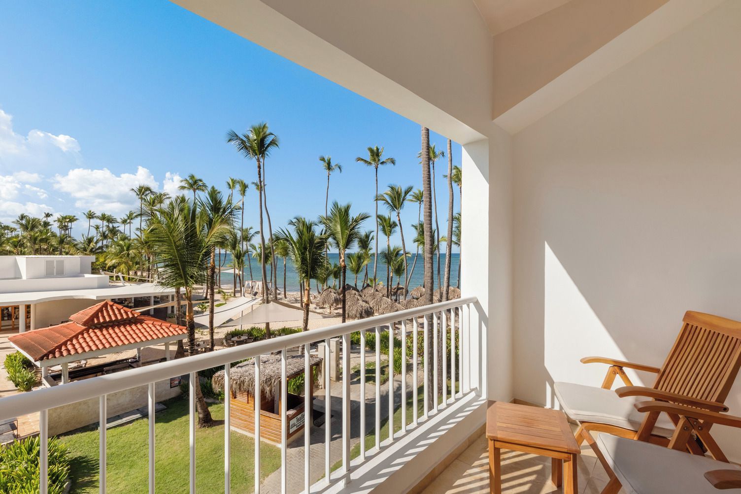 A balcony with a view of a beach, palm trees, and a pool area.
