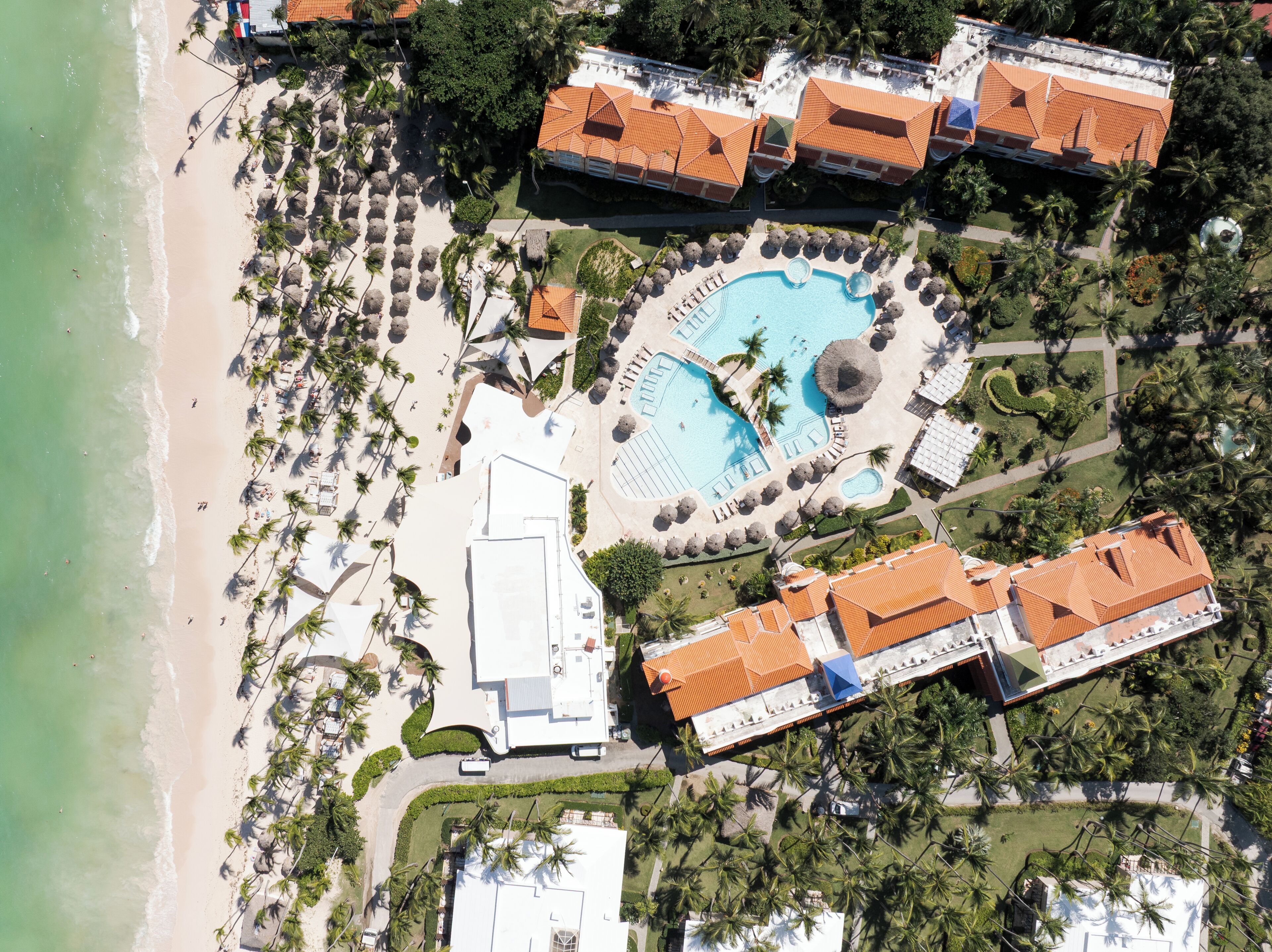 Vue aérienne d’un complexe hôtelier avec une piscine, une plage et des palmiers.