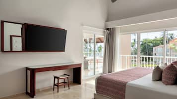 Habitación de hotel con cama, escritorio, silla, televisión y balcón con vistas al exterior.