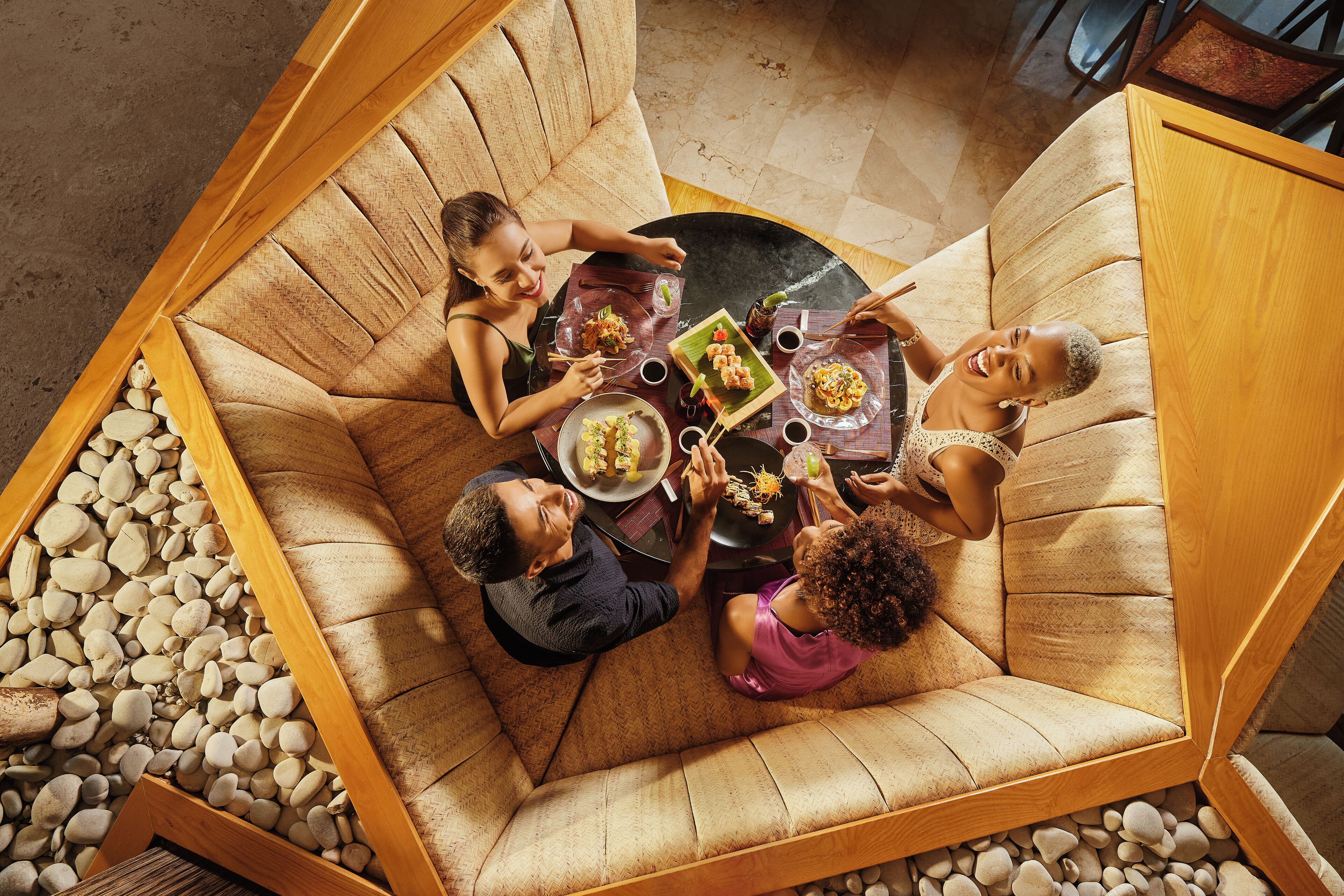 Un groupe de personnes est assis à une table dont le plateau présente un motif géométrique original, et l’ensemble est entouré d’une zone bordée de pierres.
