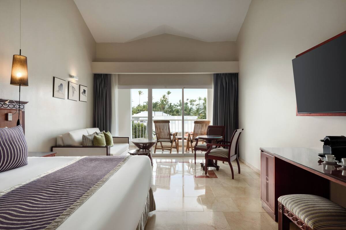A hotel room with a bed, a desk, a chair, a sofa, and a balcony with a view.