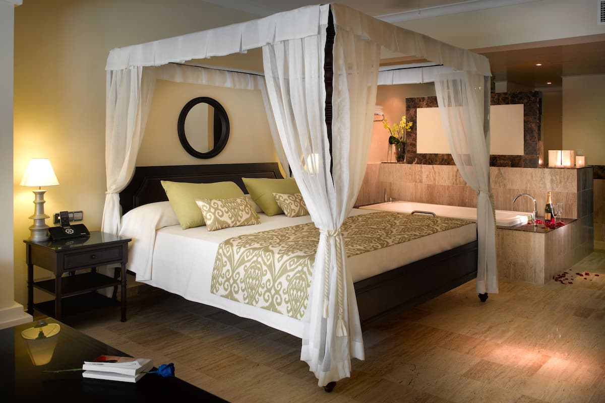 A four-poster canopy bed with a nightstand, a bedside lamp, and a mirror on the wall.