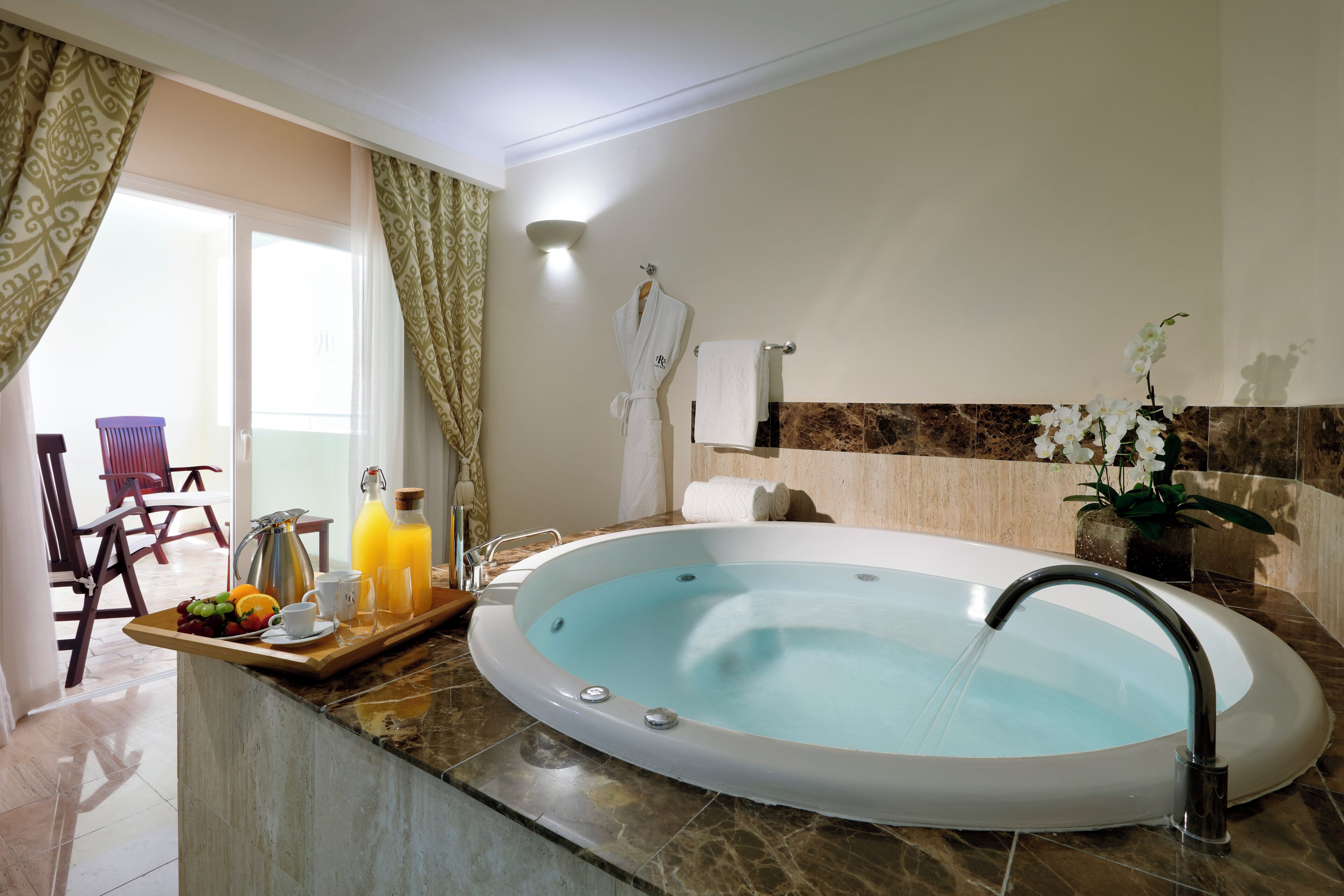Une salle de bain avec une baignoire, un porte-serviettes et un plateau contenant des fruits et une bouteille de jus d’orange.