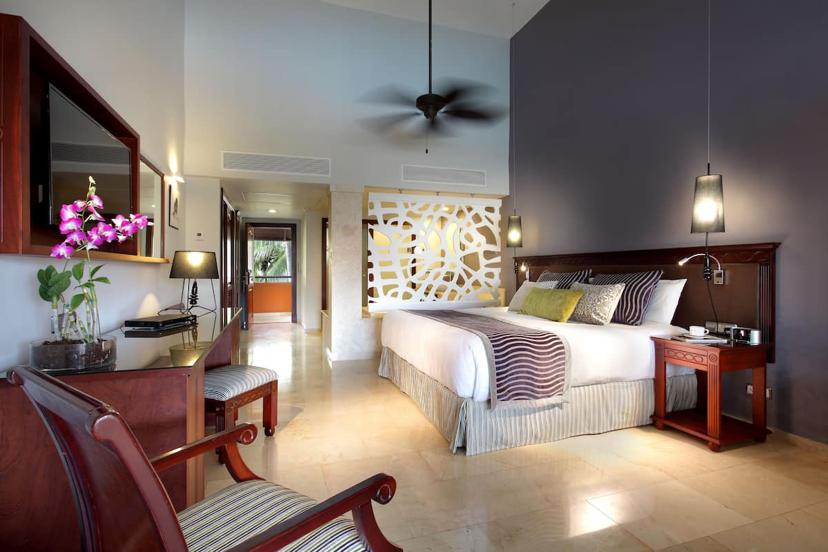 A hotel room with a bed, bedside table, chair, and a large mirror.