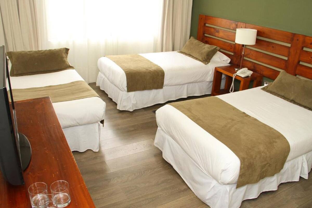 Ein Hotelzimmer mit zwei Betten, einem Holz-Kopfteil, einem Nachttisch mit Lampe und einem Fernseher.