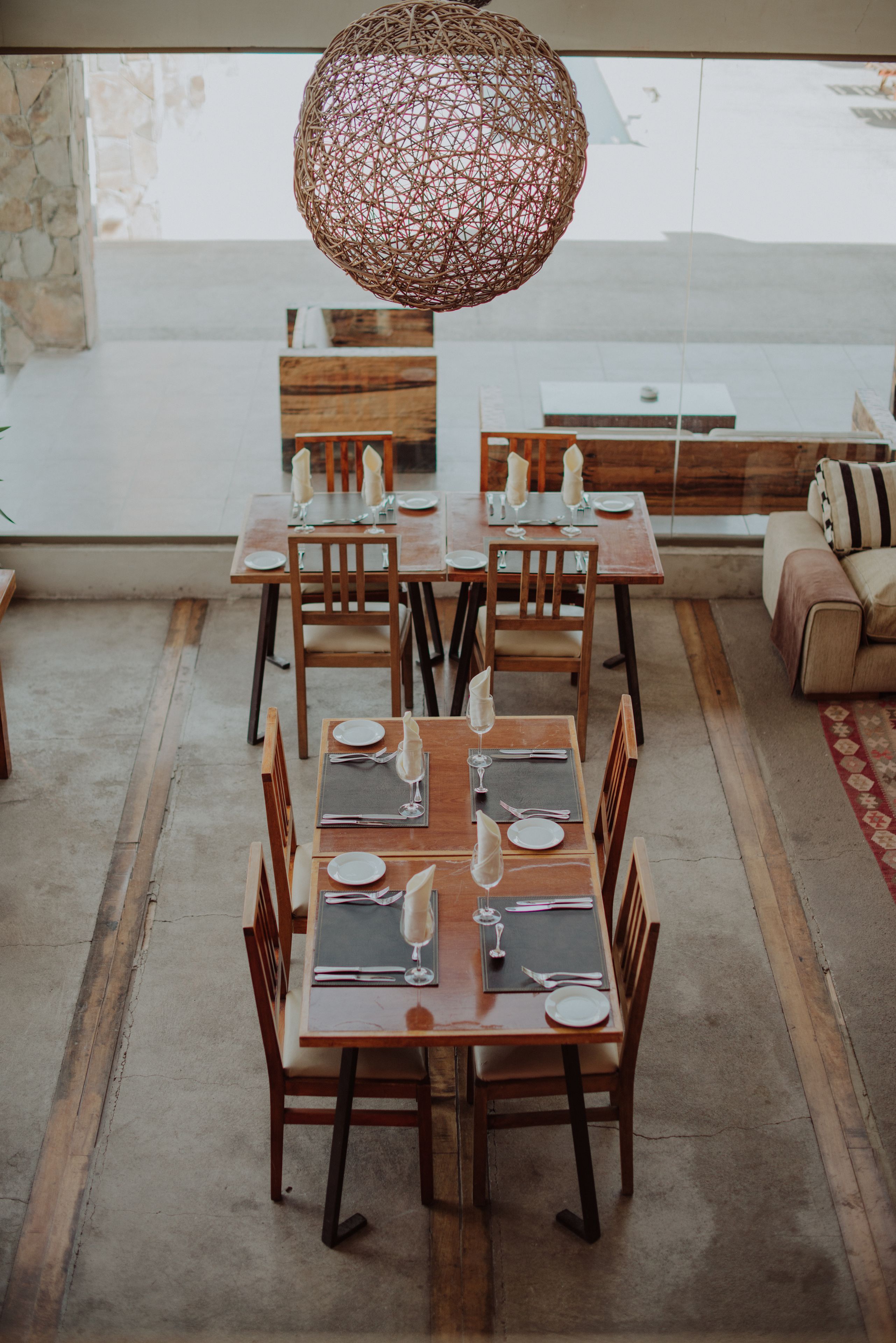 Un comedor con una lámpara central redonda, mesas de madera y sillas dispuestas para una comida.