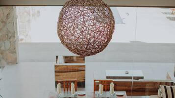 Un comedor con una lámpara central redonda, mesas de madera y sillas dispuestas para una comida.