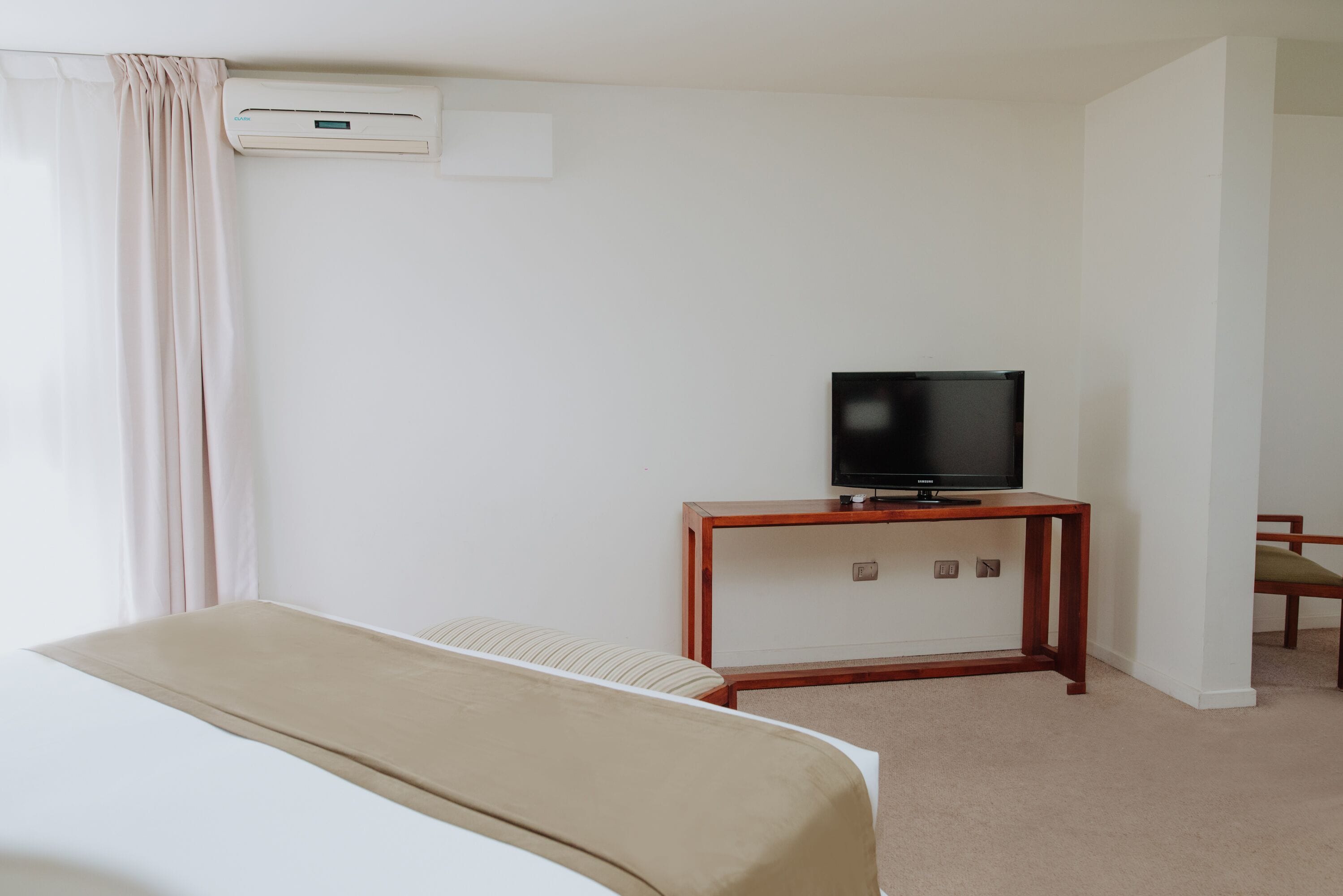 A hotel room with a bed, a television on a wooden stand, and an air conditioning unit on the wall.