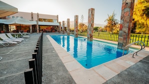 A swimming pool with lounge chairs and umbrellas, surrounded by stone pillars and a fence.