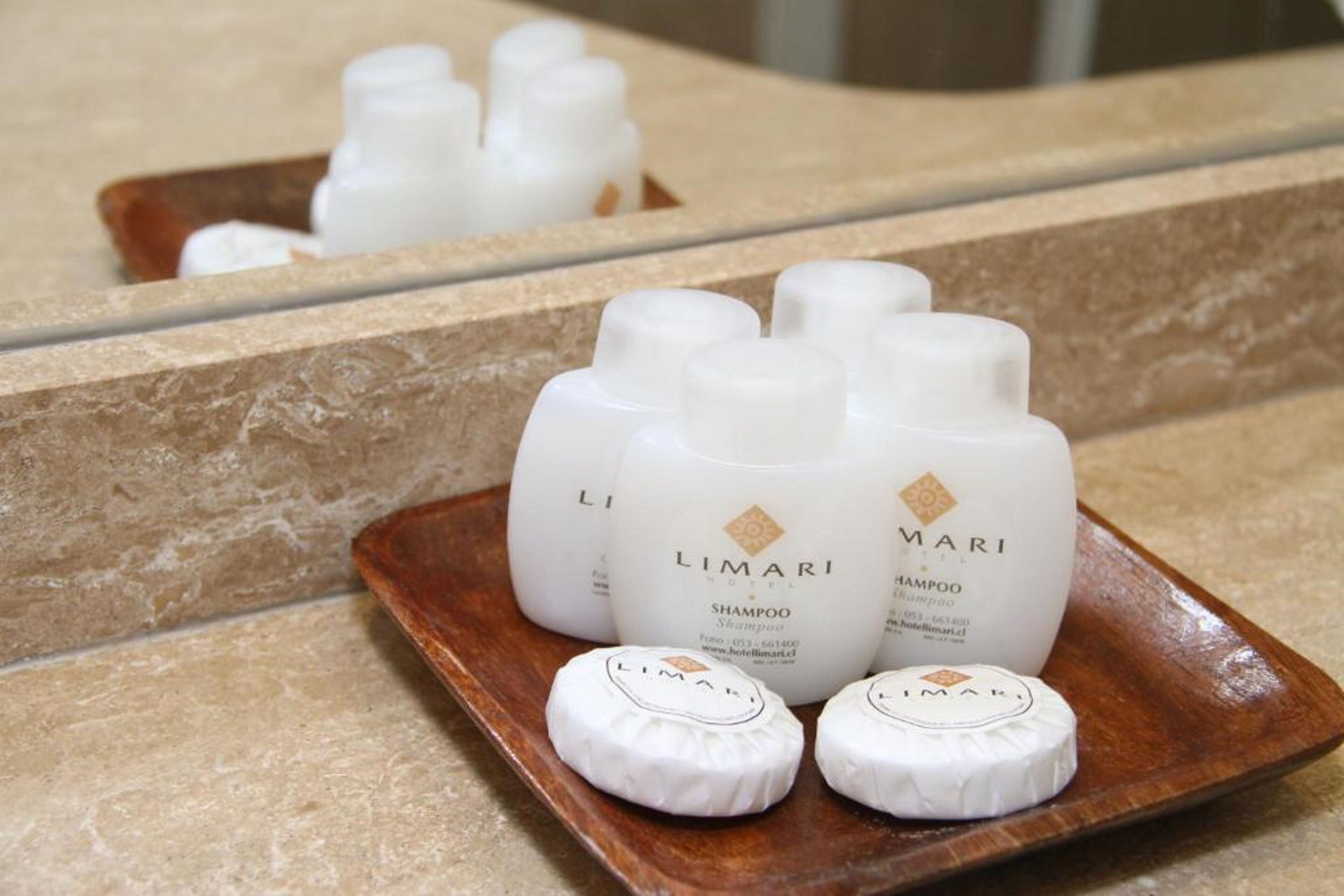 Un plateau sur lequel on trouve plusieurs bouteilles de shampoing de l’hôtel Limiari et deux petits récipients ronds, le tout posé sur un plateau en bois.