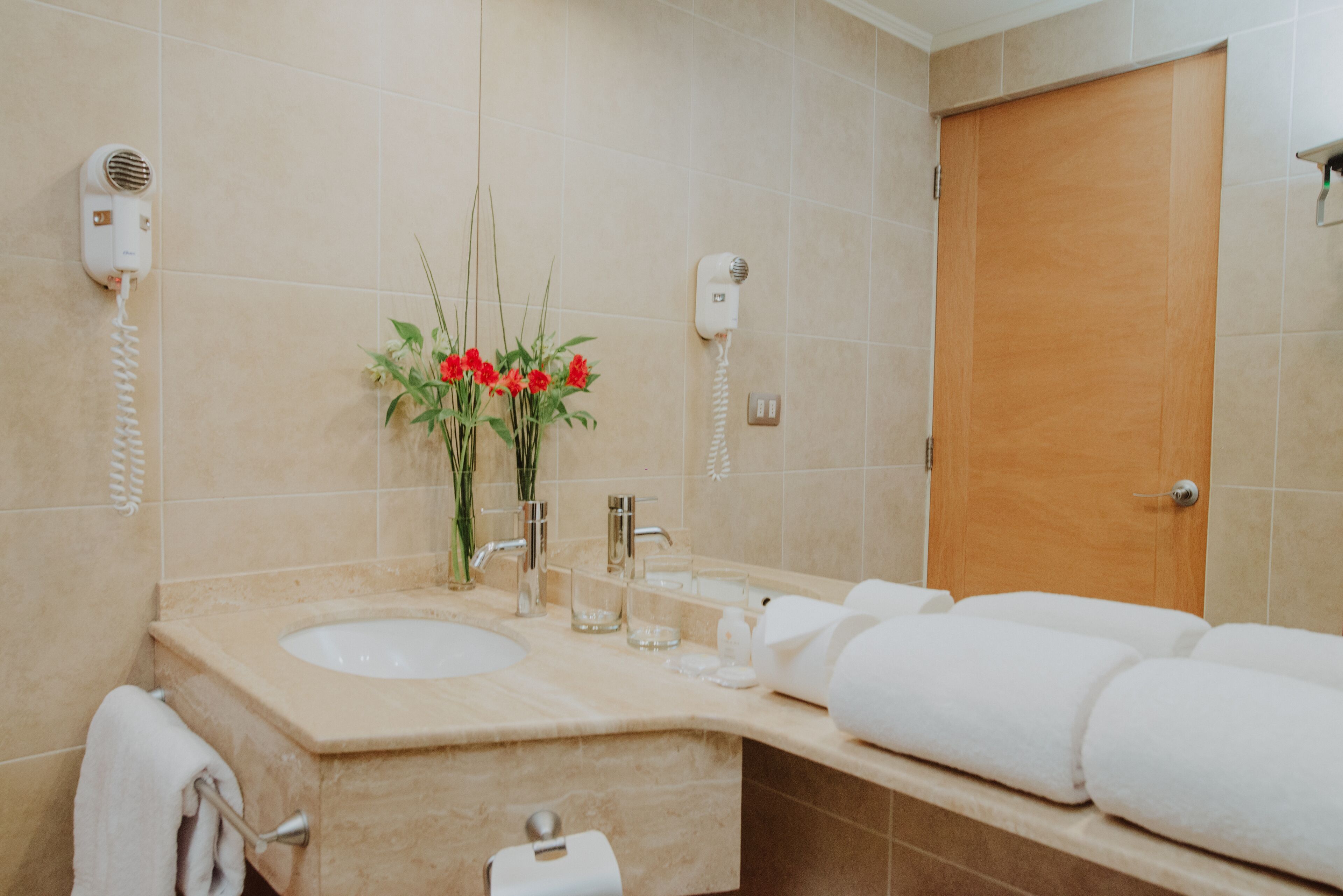 Un baño con lavamanos, espejo, toallero y una puerta de madera.