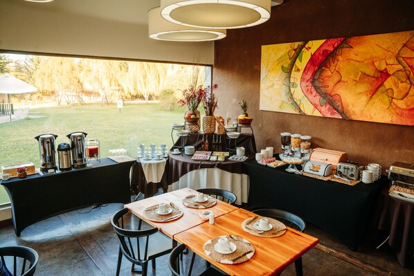 A dining area with tables set for breakfast, a coffee station, and a view of the garden.