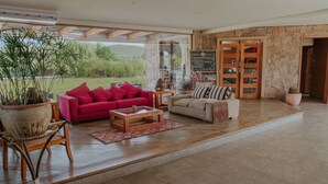 A spacious living area with a red sofa, a beige armchair, and a coffee table. There is a large window offering a view of the outdoors.