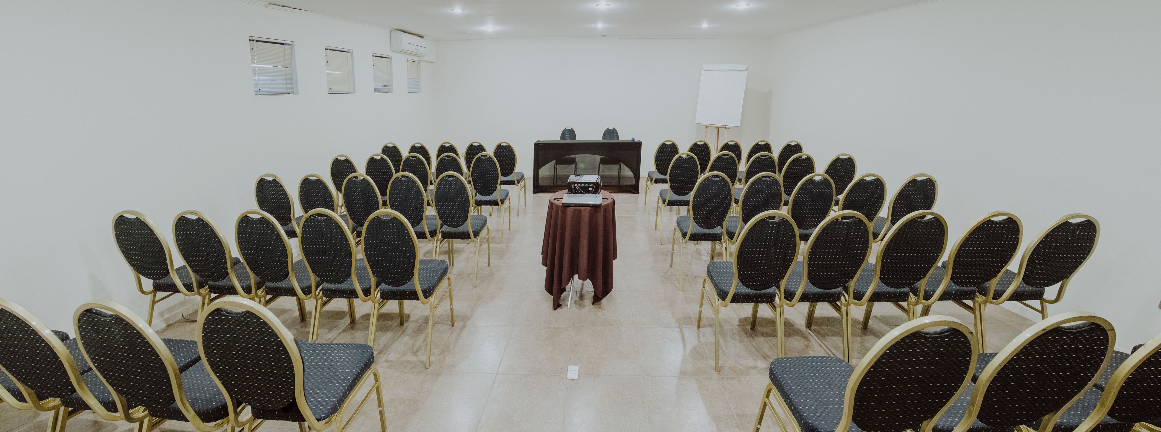 Une salle de conférence avec des rangées de chaises disposées face à un pupitre, un tableau blanc et un projecteur.