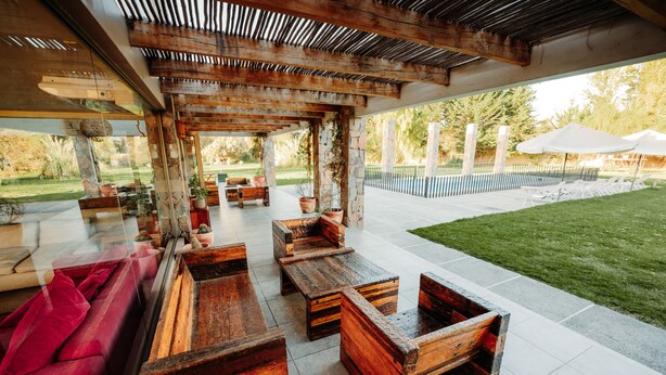An outdoor patio area with wooden furniture, a red sofa, and a view of the backyard.