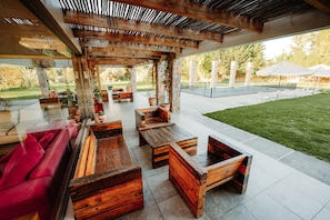 An outdoor patio area with wooden furniture, a red sofa, and a view of the backyard.