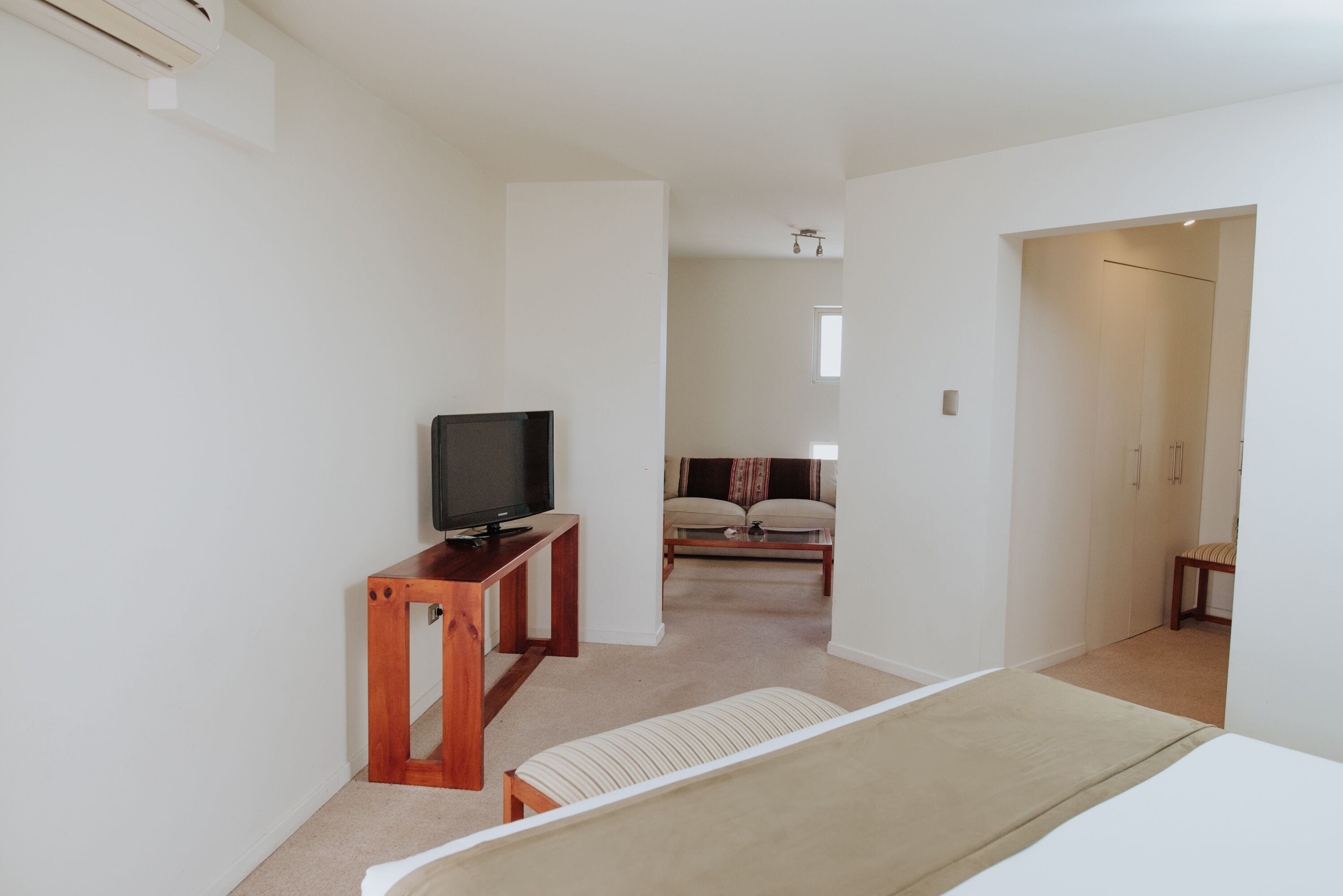 Una habitación de hotel moderna con una televisión de pantalla plana sobre un soporte de madera, un sofá y una cama con cubierta color beige.