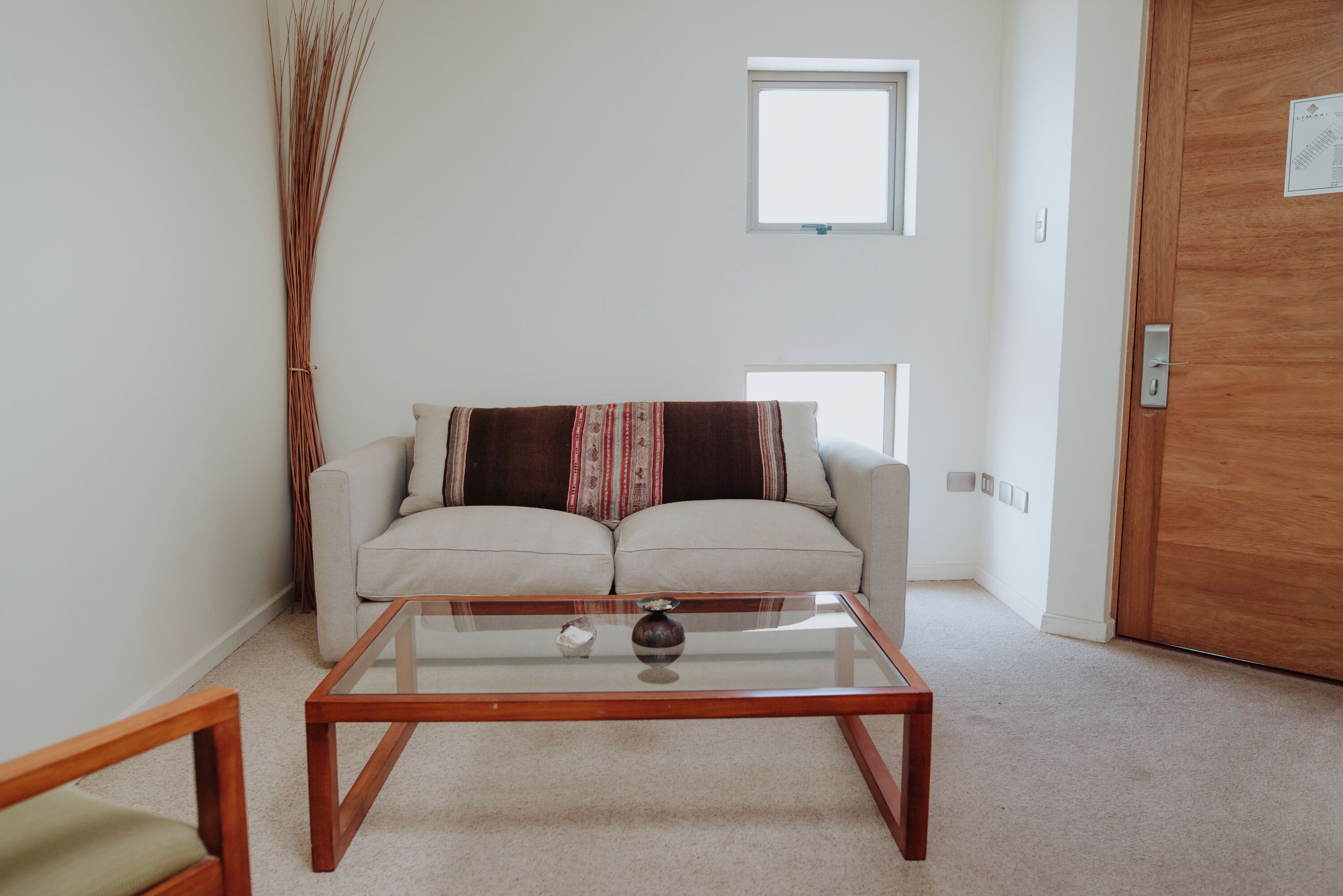 Un salon avec une table basse en verre, un canapé beige et une fenêtre.