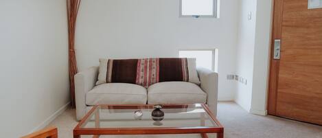 Un salon avec une table basse en verre, un canapé beige et une fenêtre.