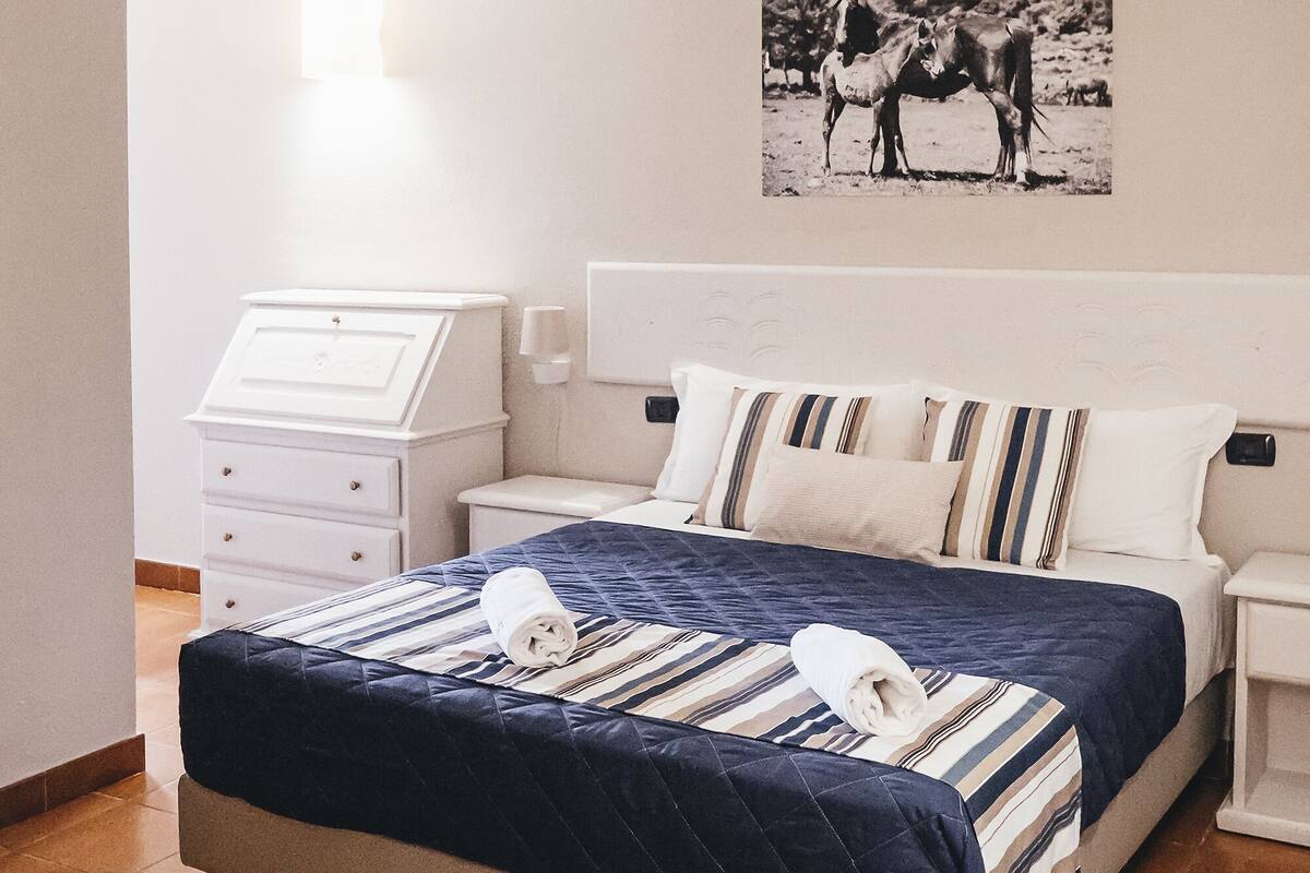 Une chambre à coucher comprenant un lit, une table de chevet, une commode et une lampe fixée au mur.