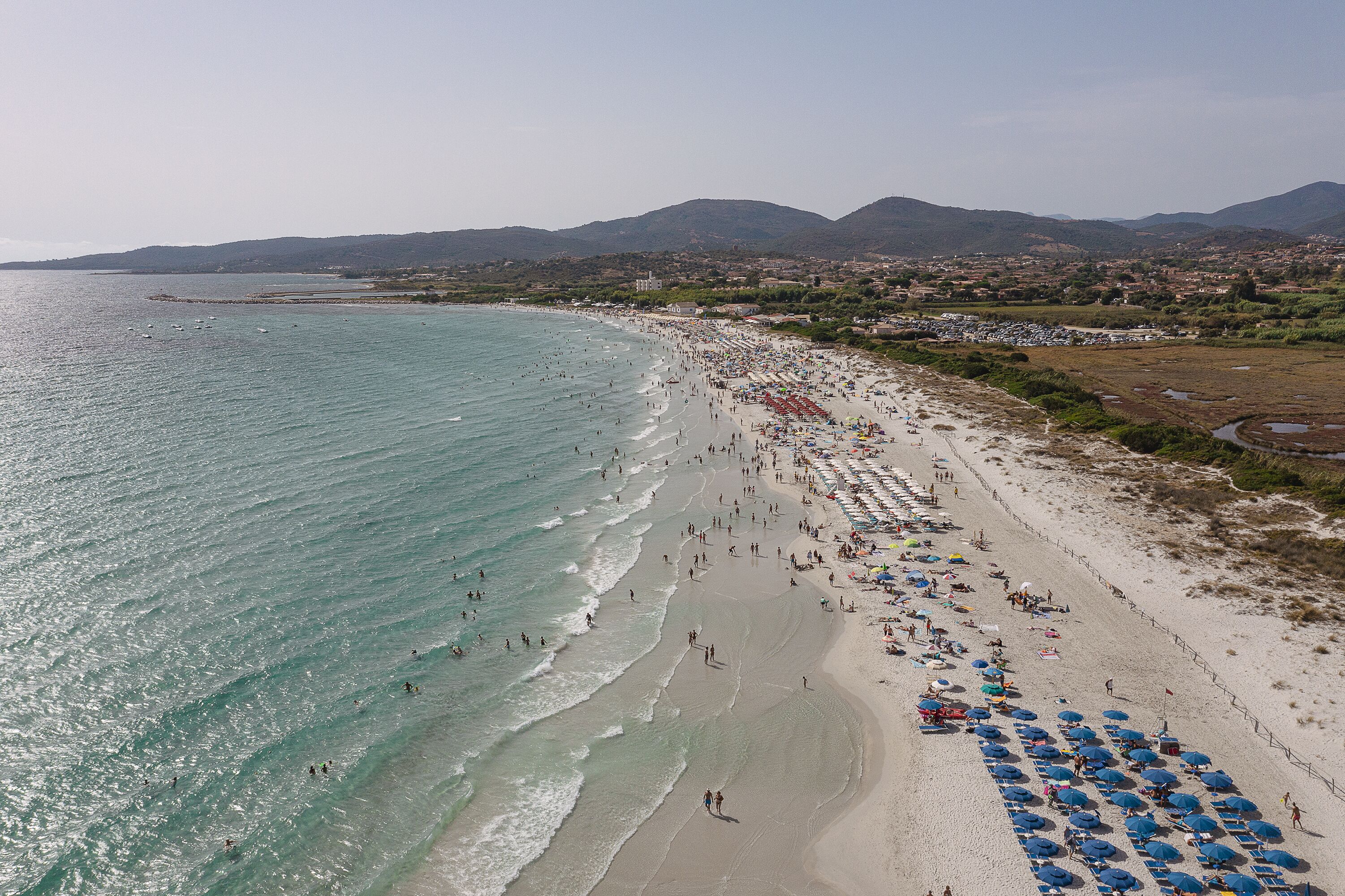 Une plage avec une longue étendue de sable, quelques parasols et des gens.