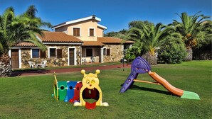 Ein Haus mit Steinverkleidung, einem Ziegeldach und einem Vorgarten mit Spielplatz und Palmen.