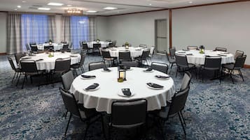 A conference room with multiple round tables, each with chairs and white tablecloths.