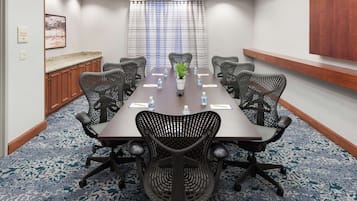 A conference room with a long table, six chairs, a potted plant, water bottles, and a framed picture on the wall.
