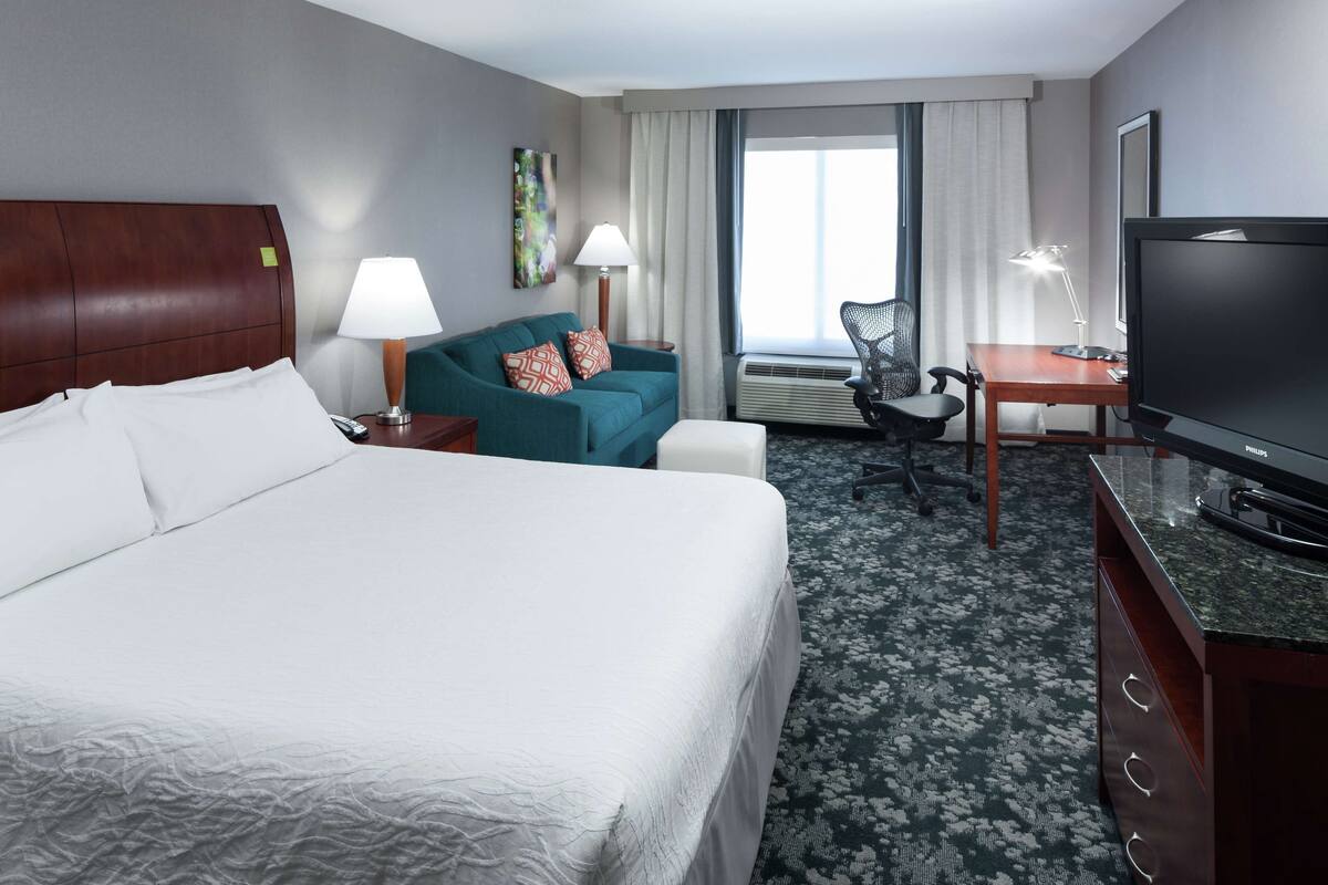 Une chambre d’hôtel avec un grand lit, un bureau avec un ordinateur, une télévision et une chaise.