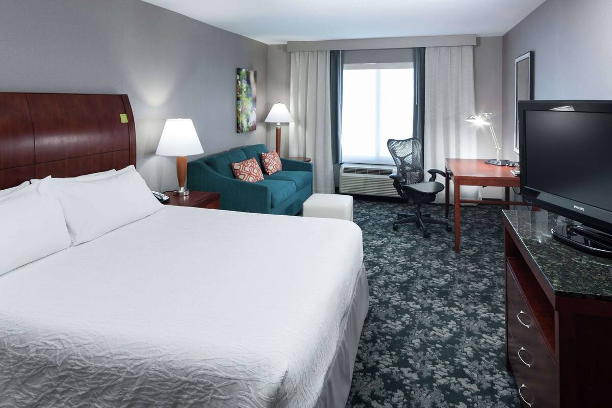 Une chambre d’hôtel équipée d’un lit, d’un bureau, d’une télévision, d’une chaise et d’une fenêtre avec des rideaux.