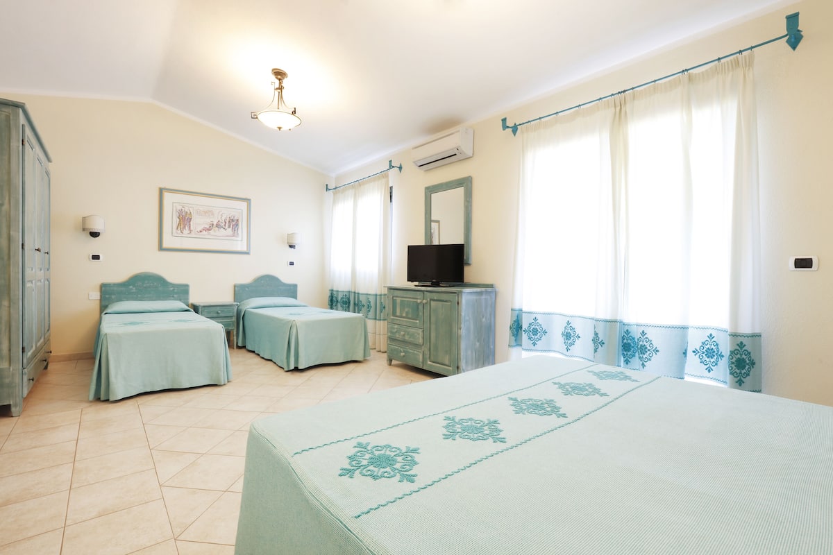 A bedroom with two single beds, a large bed, a TV on a dresser, and a window with curtains.