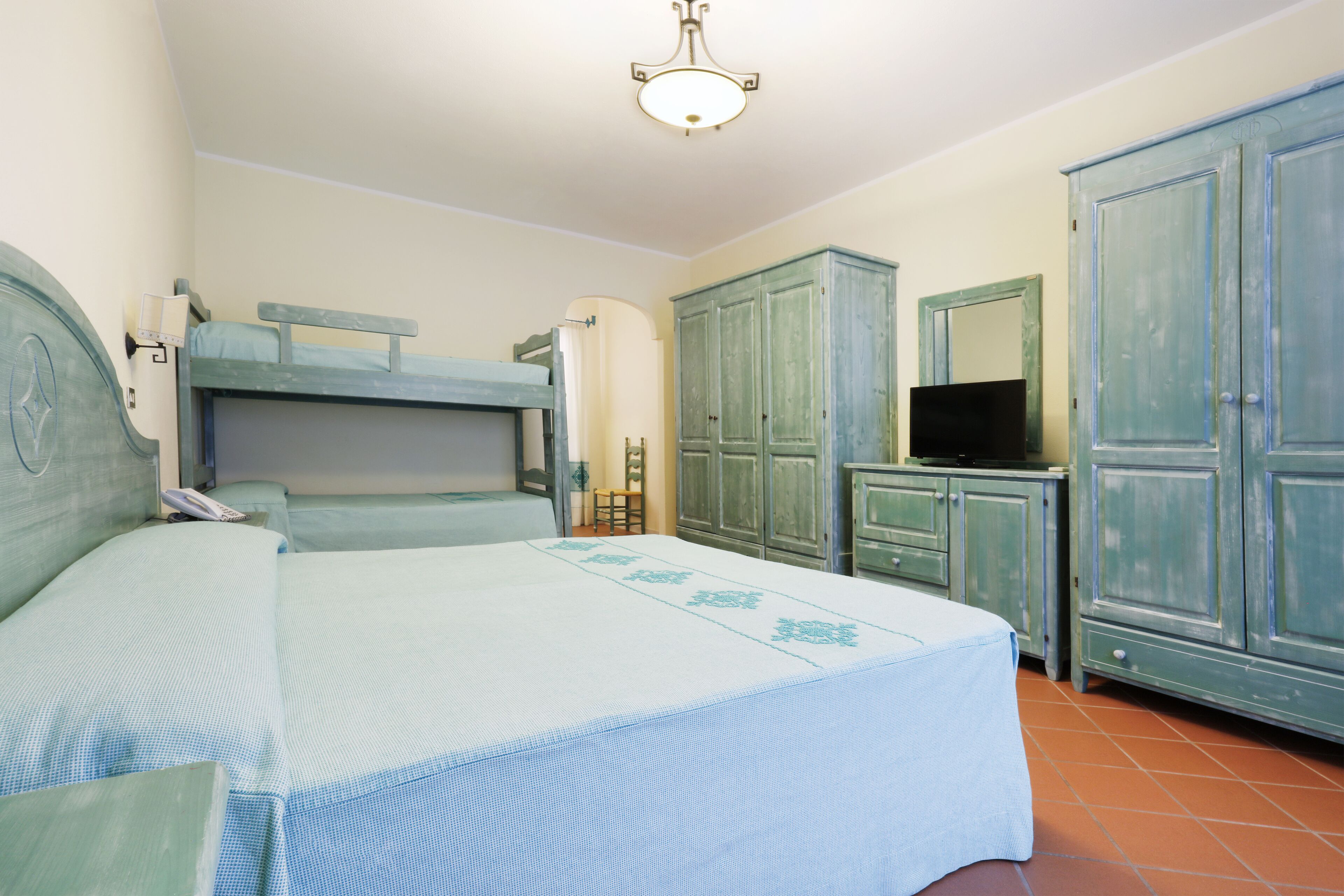 A bedroom with a bunk bed, a desk with a television, and a wardrobe.