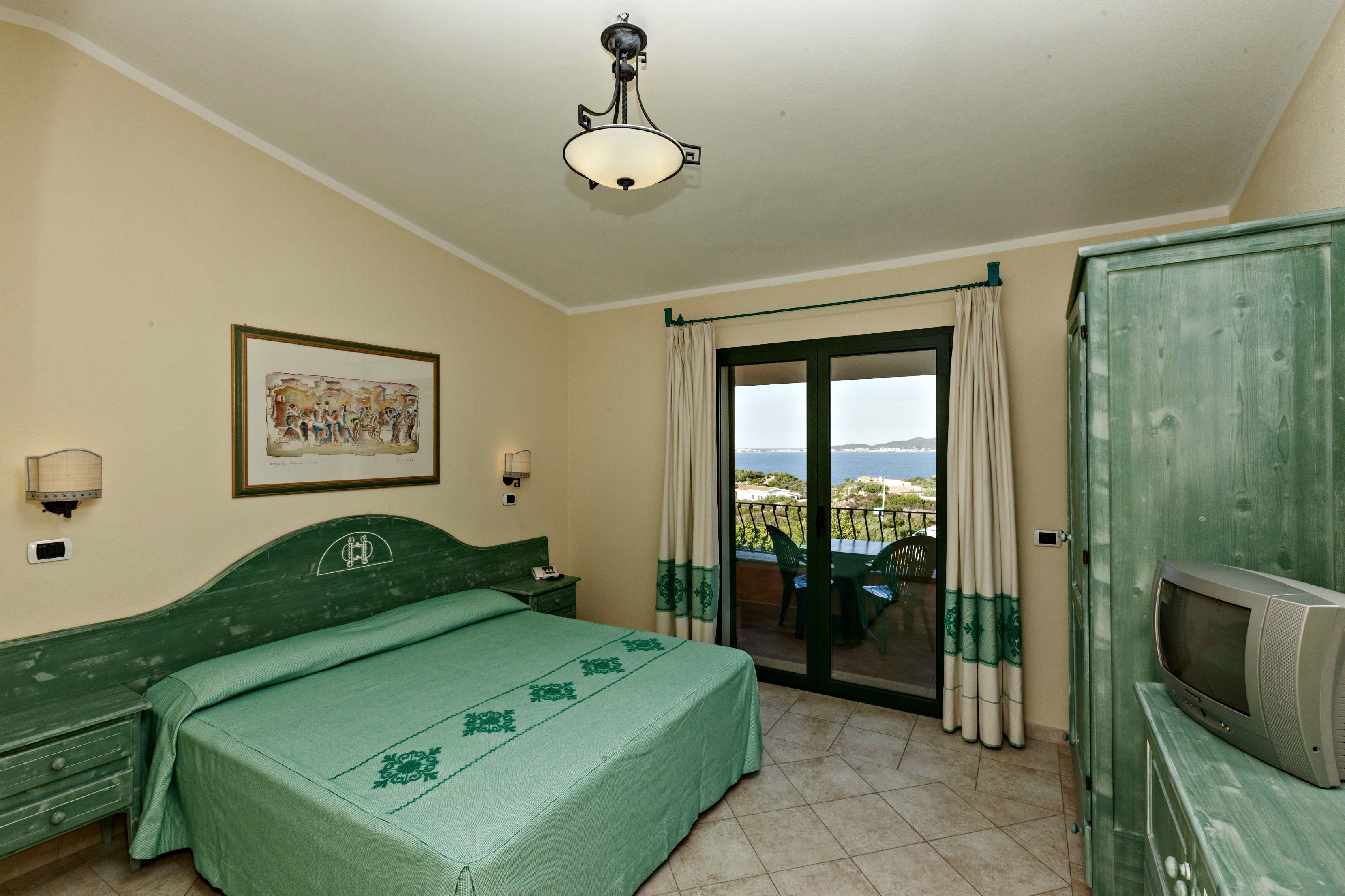 Une chambre à coucher avec un lit, une télévision, un tableau et une vue sur la mer, visible à travers une porte coulissante.