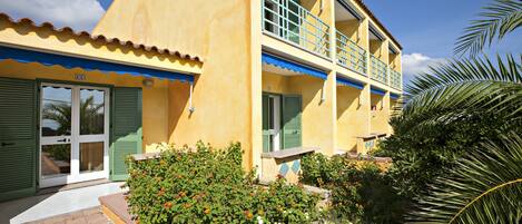 A two-story building with a yellow facade, green shutters, and a balcony with blue railings.