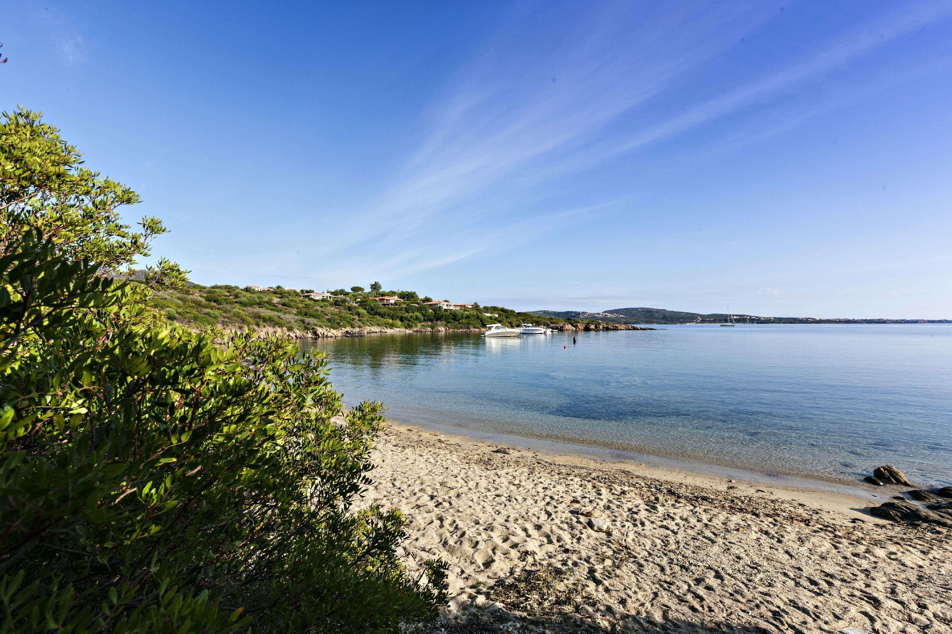 A beach with clear skies, calm water, and boats in the distance.