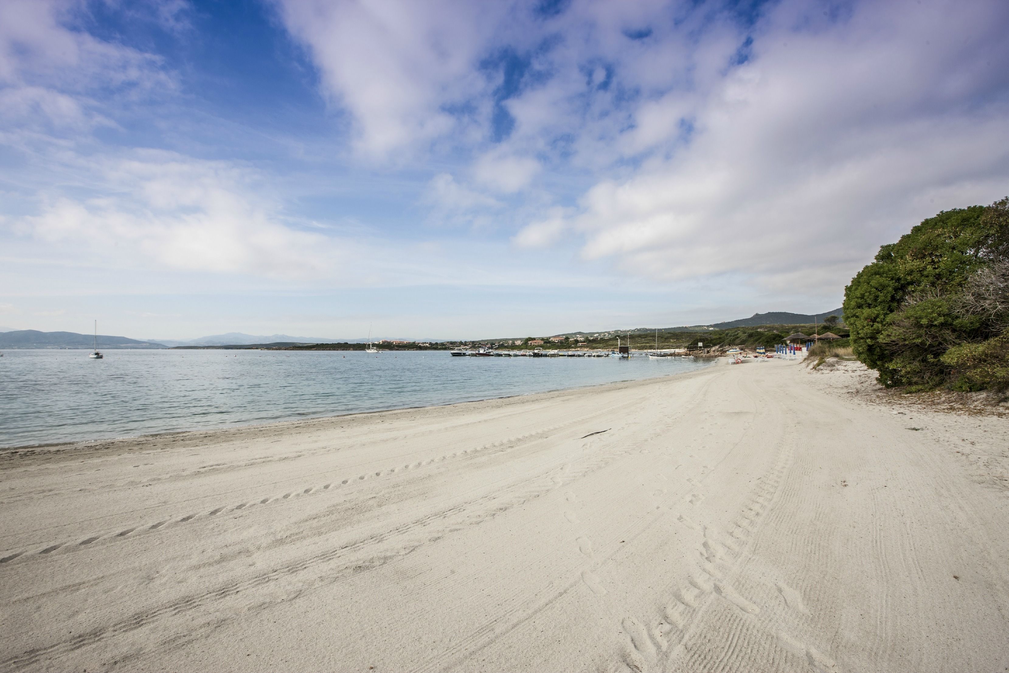 A beach with a sandy shore, calm water, and distant hills.