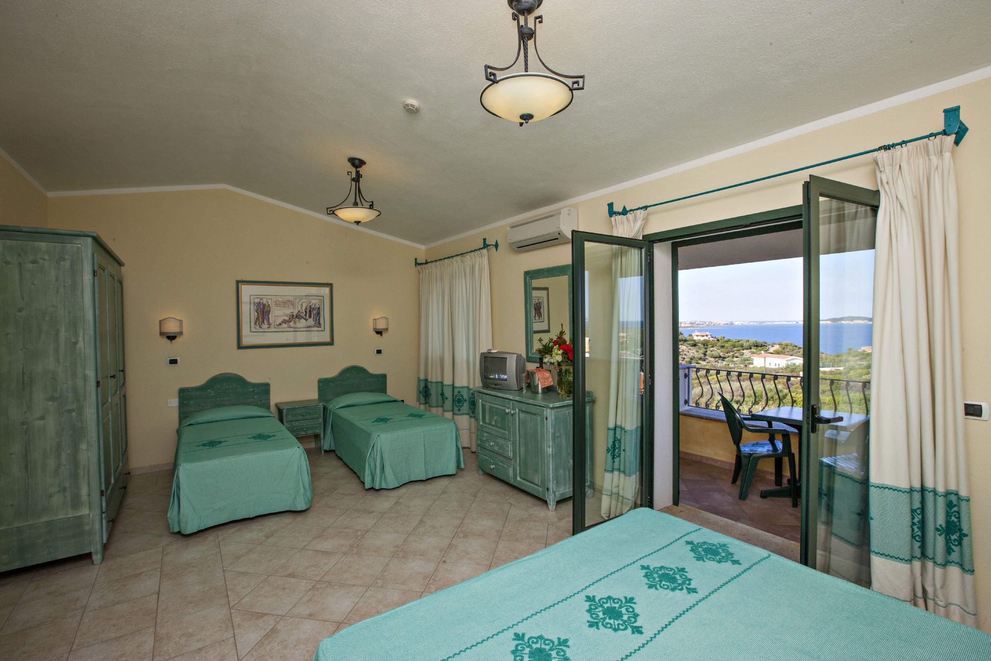A bedroom with two single beds, a TV, a dresser, and a balcony with a view.