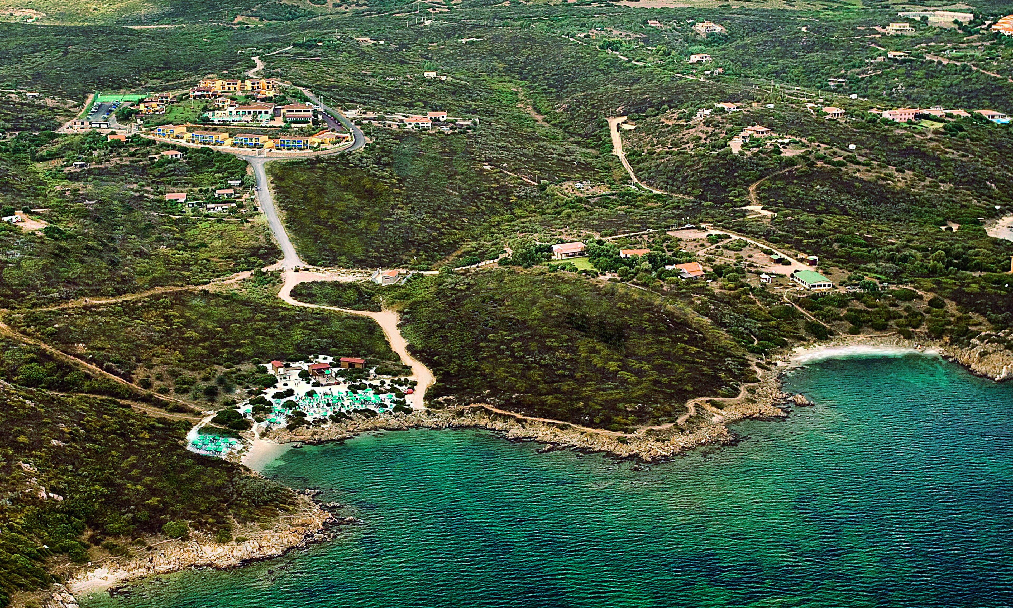 Vue aérienne d’une station balnéaire, avec un bâtiment central entouré de villas, reliées par des allées, et une plage parsemée de parasols.
