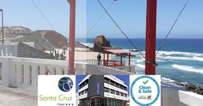 A coastal hotel with a view of the ocean, a red and white structure, and a sign indicating 'Clean & Safe' and 'Tourism of Portugal'. - Hotel Santa Cruz (Torres Vedras)