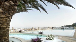 Zona de piscina con sillones de descanso y vista a barcos al fondo.