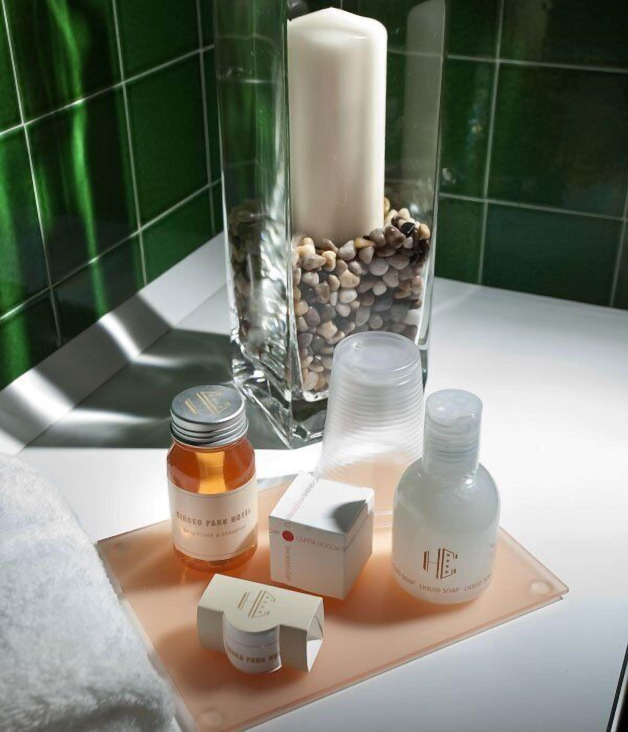 Un baño con un recipiente de vidrio que contiene una vela, un frasco de loción, una botella de jabón y una caja de pañuelos.