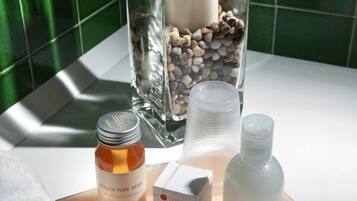 Un baño con un recipiente de vidrio que contiene una vela, un frasco de loción, una botella de jabón y una caja de pañuelos.