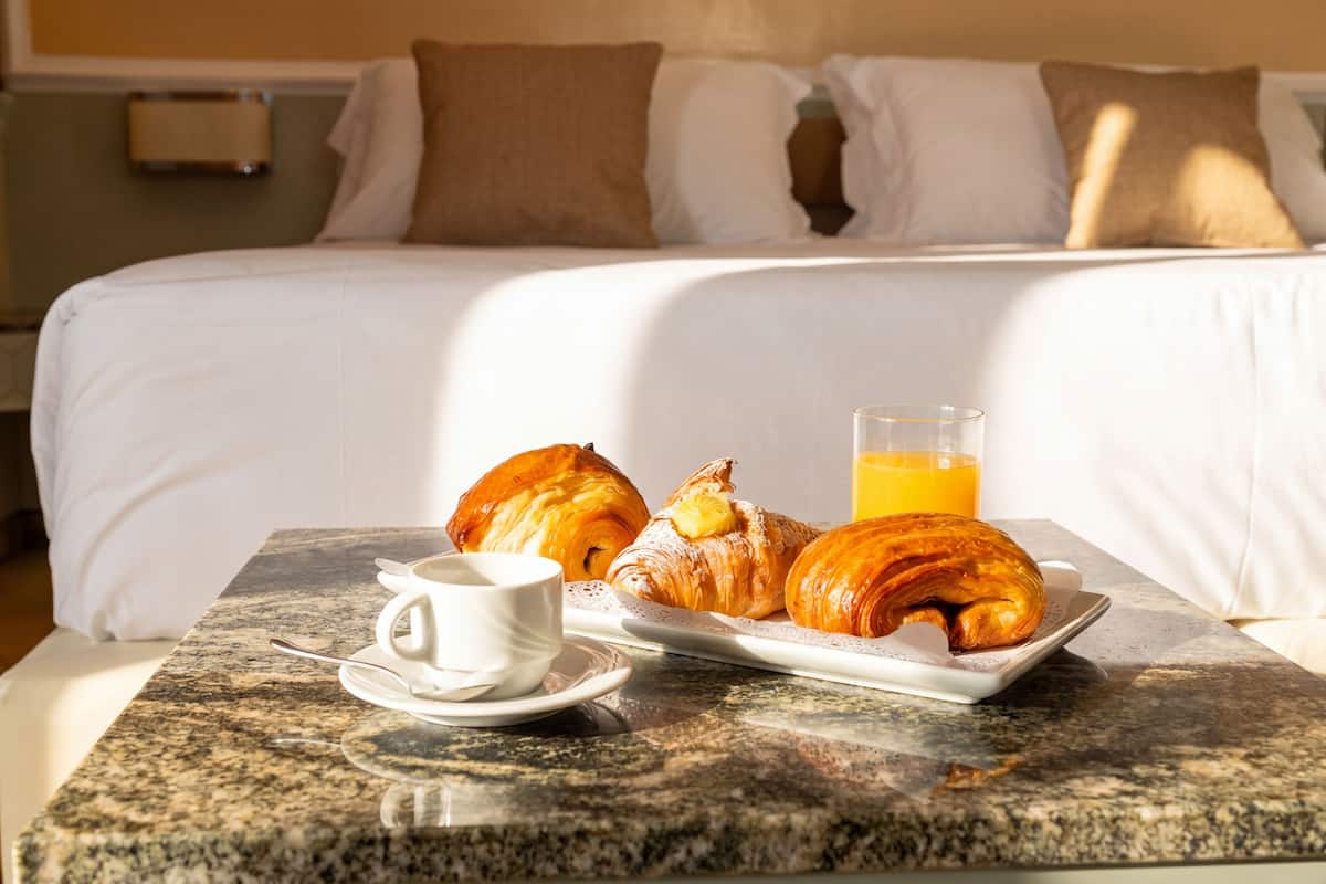 Un plateau de petit-déjeuner avec des croissants, une tasse de café et un verre de jus d’orange, posé sur une table en marbre dans une chambre d’hôtel.